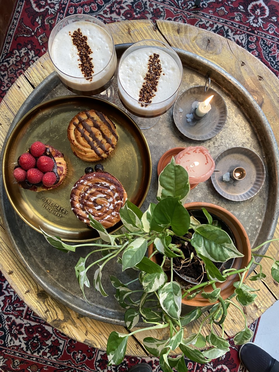A table with two espresso martinis, a candle, a plant and cinnamon buns.